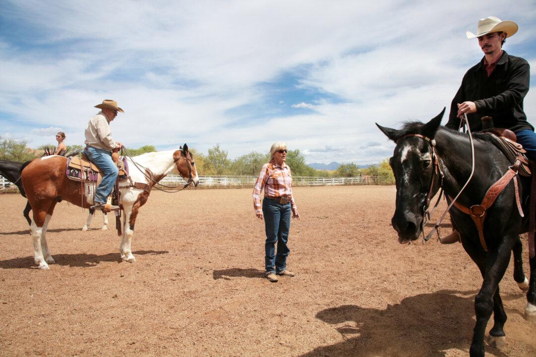 Arizona Cowboy College owner Lori Bridwell watches the progress of the attendees on horseback from the center of the arena at the college's facility in Scottsdale, Ariz., on April 13, 2026. (Richard Moore/The Epoch Times)