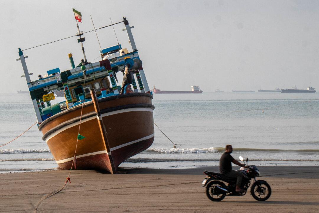 TOPSHOT - In this picture obtained from Iran's ISNA news agency on April 24, 2026, an Iranian man rides his motorcycle past a boat at Suru Beach in Bandar Abbas along the Strait of Hormuz. (Photo by RAZIEH POUDAT / ISNA / AFP via Getty Images)