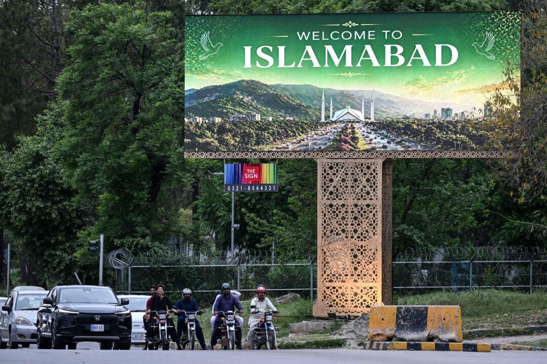 Commuters wait at a traffic signal beside a digital screen in Islamabad on April 24, 2026. Iran's state media confirmed that Foreign Minister Abbas Araghchi would travel on April 24 to Pakistan, which has been mediating between the Islamic Republic and the United States in a bid to end the Middle East war. (Photo by Farooq NAEEM / AFP via Getty Images)