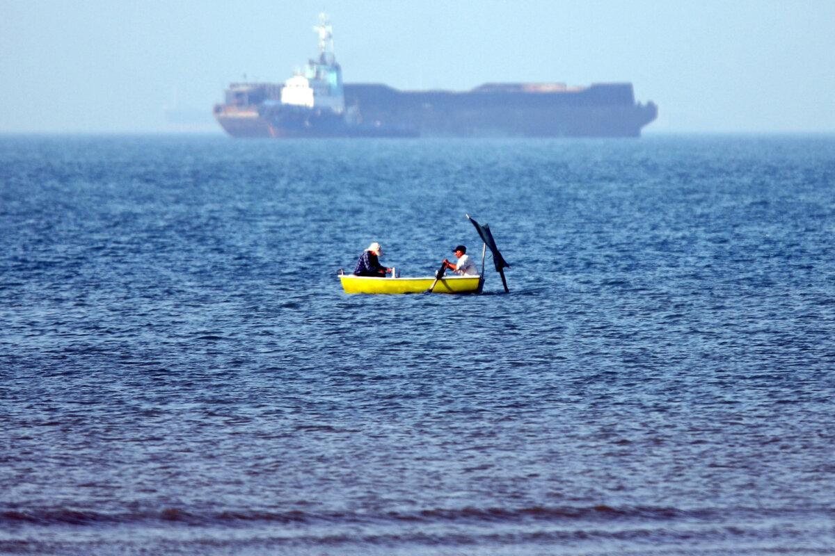 In this picture obtained from Iran's ISNA news agency on May 4, 2026, two men sitting in a skiff are seen fishing near a vessel anchored in the Strait of Hormuz off Bandar Abbas in southern Iran. (Amirhossein Khorgooei/ISNA/AFP via Getty Images)