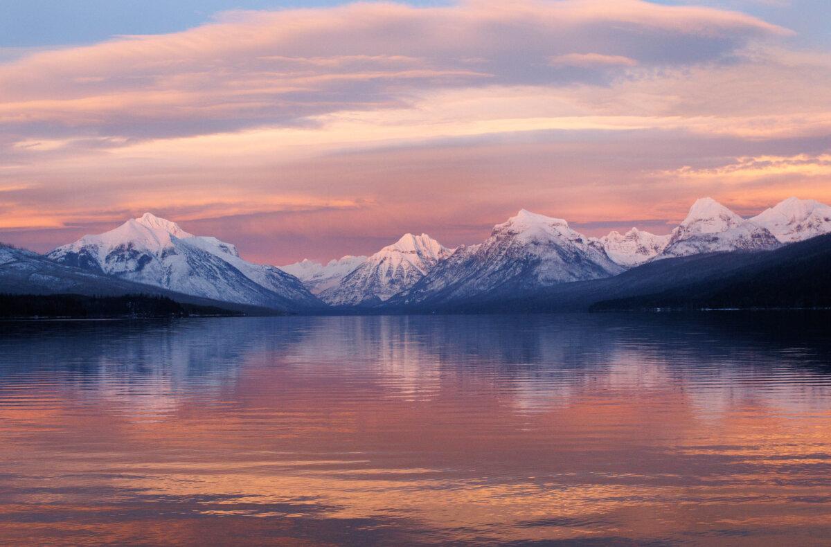 Alpenglow's rosy hue is reflected in the sky, mountains, and lake at Lake McDonald on Dec. 30, 2025. (NPS)
