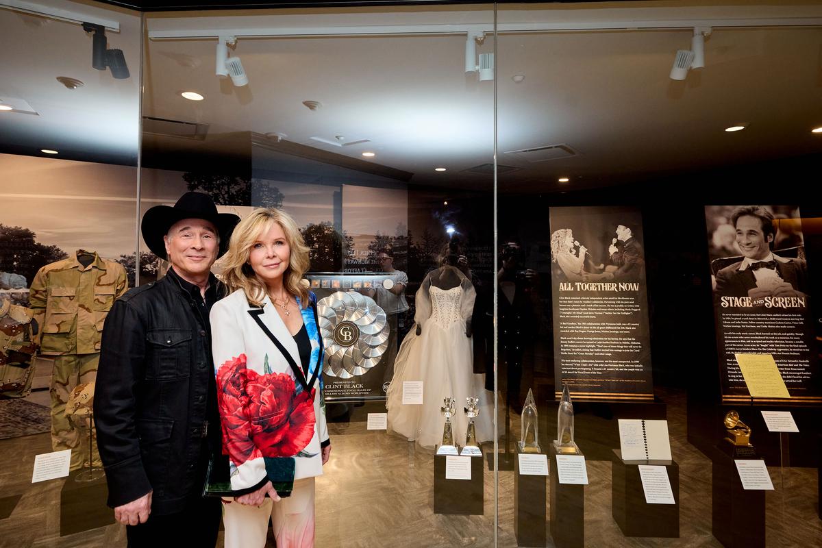 Clint Black and his wife Lisa Hartman Black, actress and singer, pose in front of the exhibition display with the Brides International dress that Lisa wore in their duet music video for “When I Said I Do." (Caroline Russell/Country Music Hall of Fame and Museum)