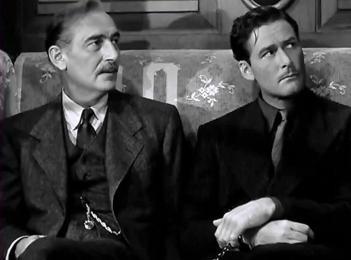 Marcel Bonet (Paul Lukas, L) keeps a watchful eye on Jean Picard (Errol Flynn), in “Uncertain Glory.” (Warner Bros.)