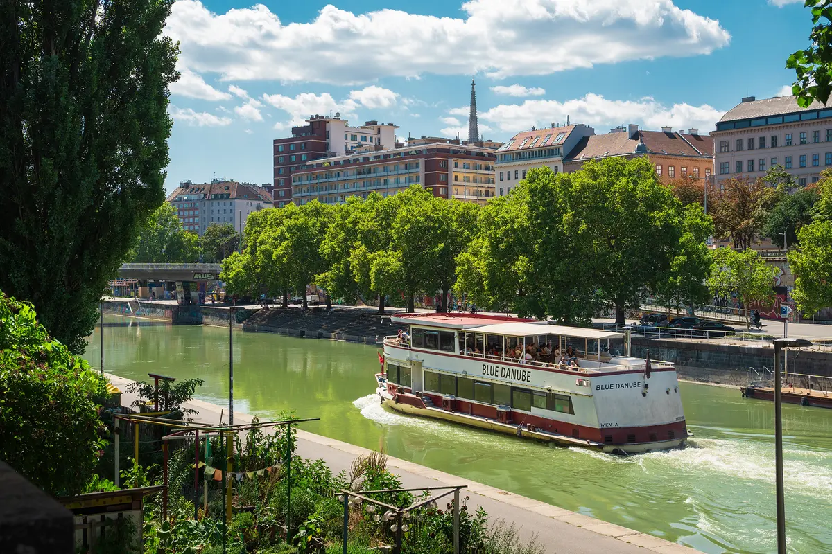 A river cruise sails along the Danube Canal. The spire of St. Stephen's Cathedral can be seen in the background. (Lomb/Shutterstock)