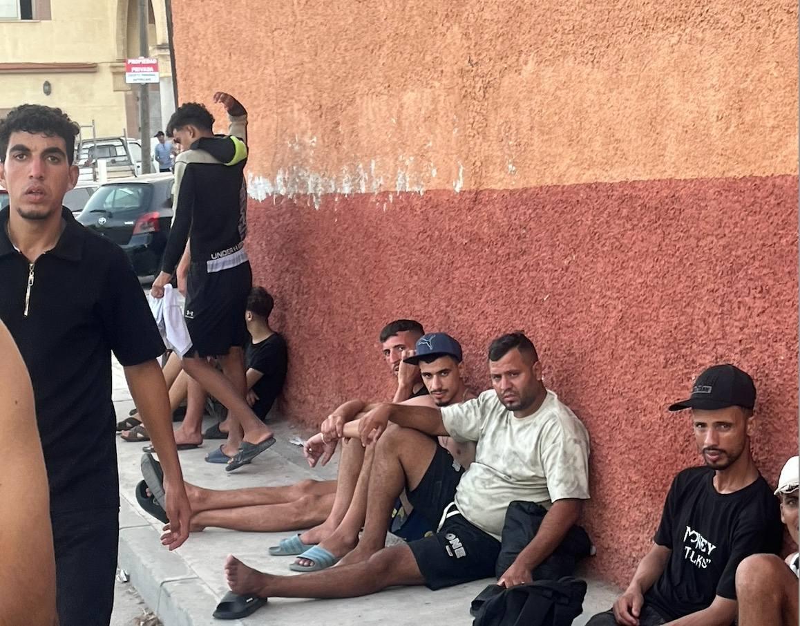 Moroccan migrants rest after arriving from Morocco along a sidewalk against a wall in Ceuta, July 31, 2026. (Etienne Fauhaire/The Epoch Times)