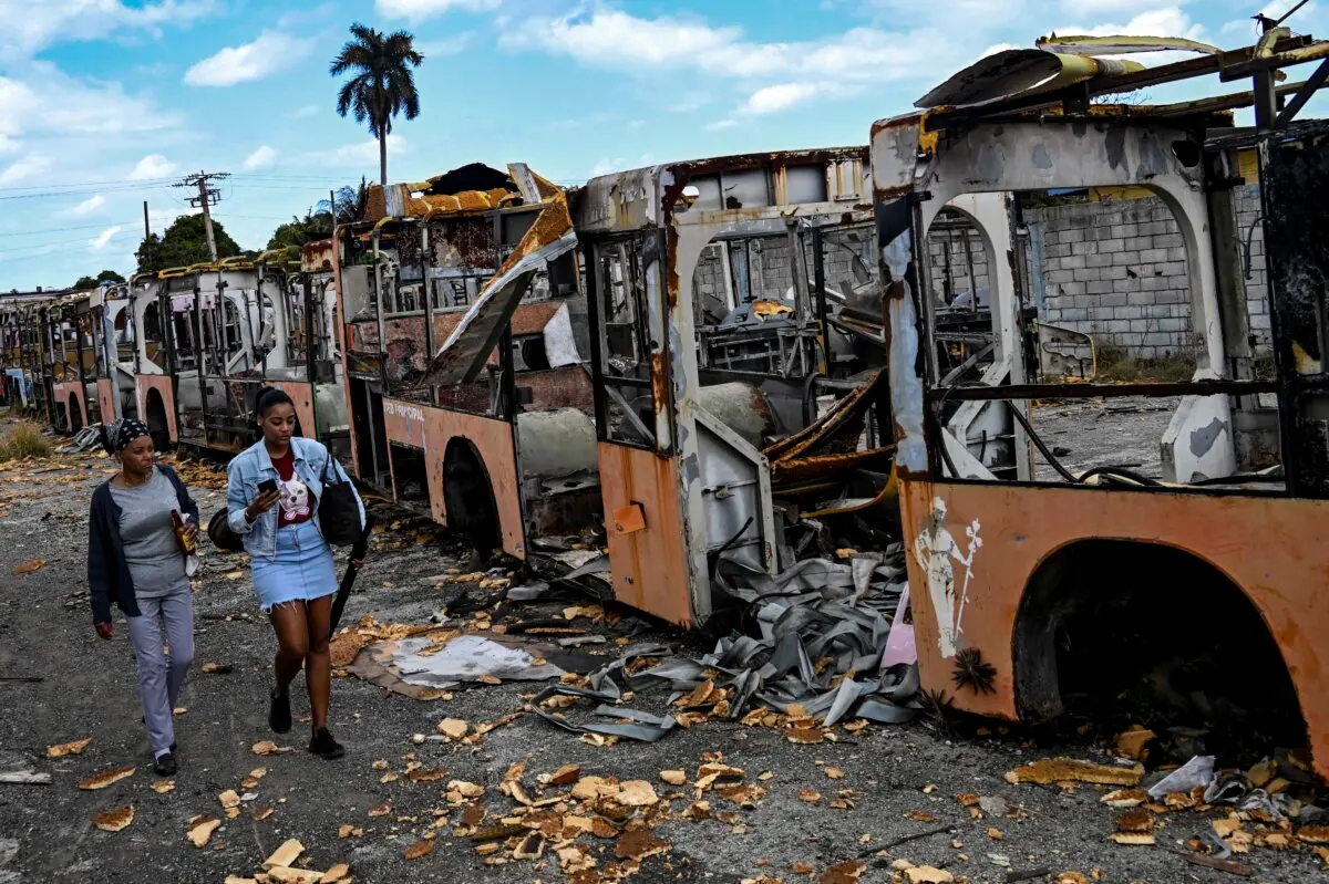 Women walk past stripped, derelict bus carcasses parked in a yard in a neighborhood in western Havana, on July 5, 2026. (Yamil Lage/AFP via Getty Images)