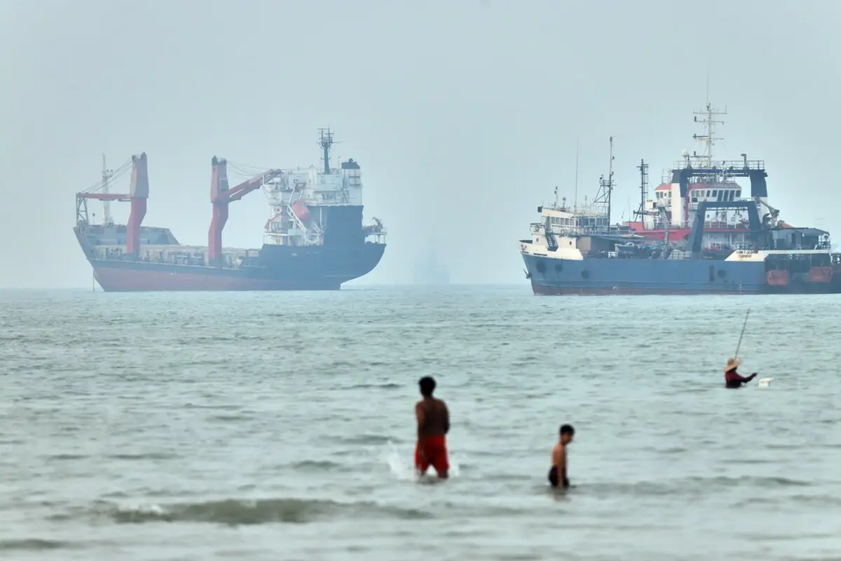 Children wade in the water with cargo ships at anchor in the background and a fisherman nearby, in the Strait of Hormuz off Bandar Abbas, Iran, on June 30, 2026. (Amirhosein Khorgooi/ISNA via AP)