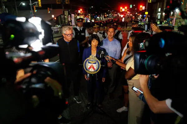 Toronto city councillor Mike Colle (left) listens as Toronto Mayor Olivia Chow addresses the media after a shooting at the Salsa on St. Clair event in Toronto, on July 11, 2026. (The Canadian Press/Keito Newman)