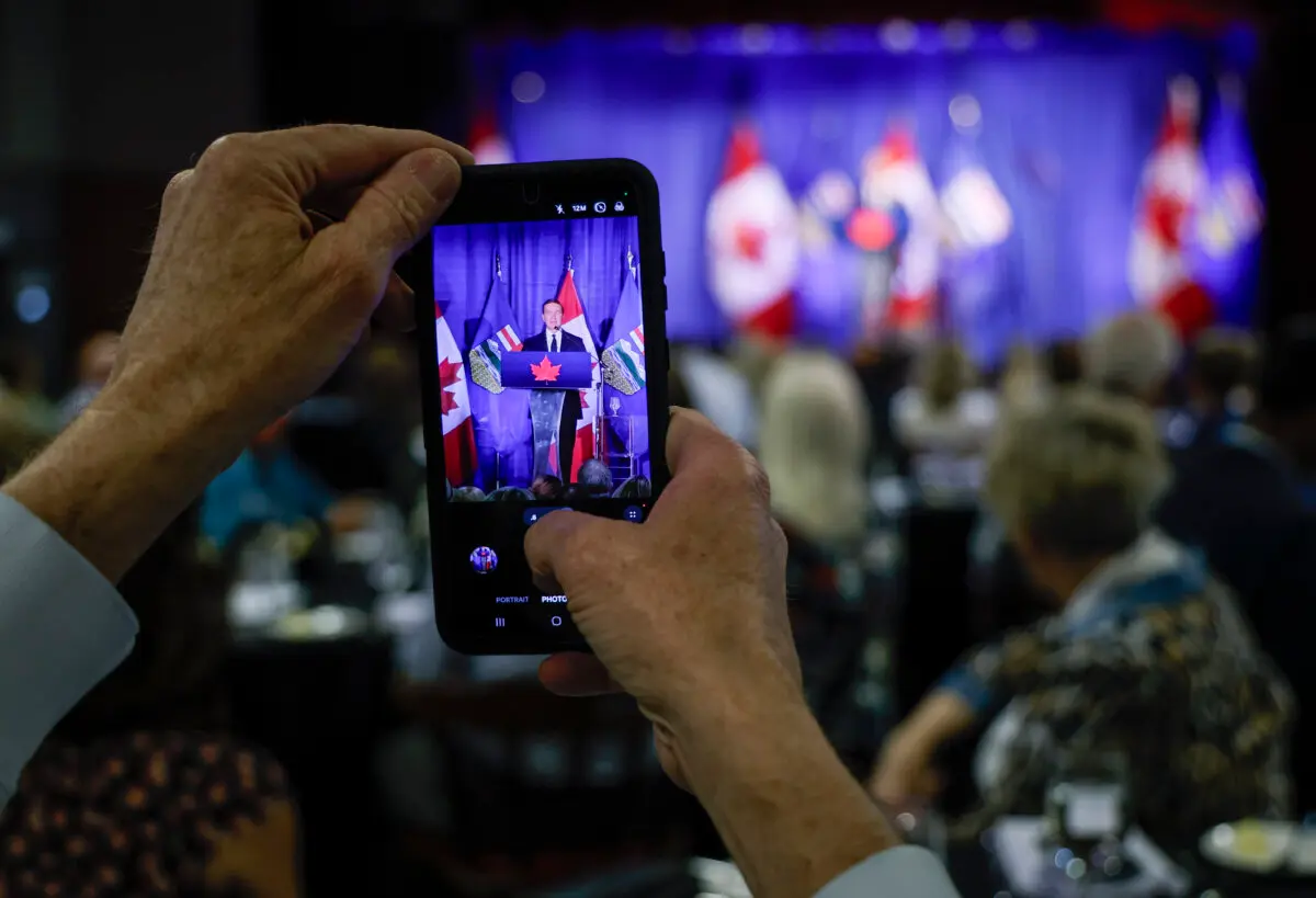 A man uses a smartphone to photograph Conservative Leader Pierre Poilievre as he delivers a speech in Calgary on June 8, 2026. (The Canadian Press/Jeff McIntosh)