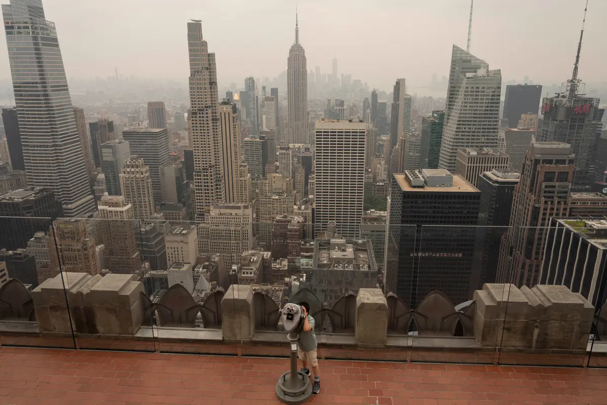 A person uses binoculars to look out amid the smoke at Top of The Rock observation deck at the Rockefeller Center in New York on July 16, 2026. (Yuki Iwamura/AP Photo)