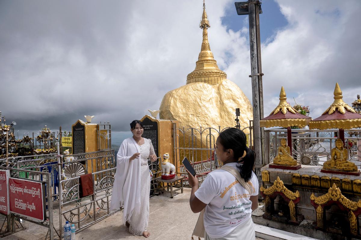 This photo taken on May 28, 2026 shows people posing for photos at the Kyite Htee Yoe Pagoda, also known as the Golden Rock Pagoda, in Mon State. (Sai Aung Main/AFP/Getty Images/TNS)