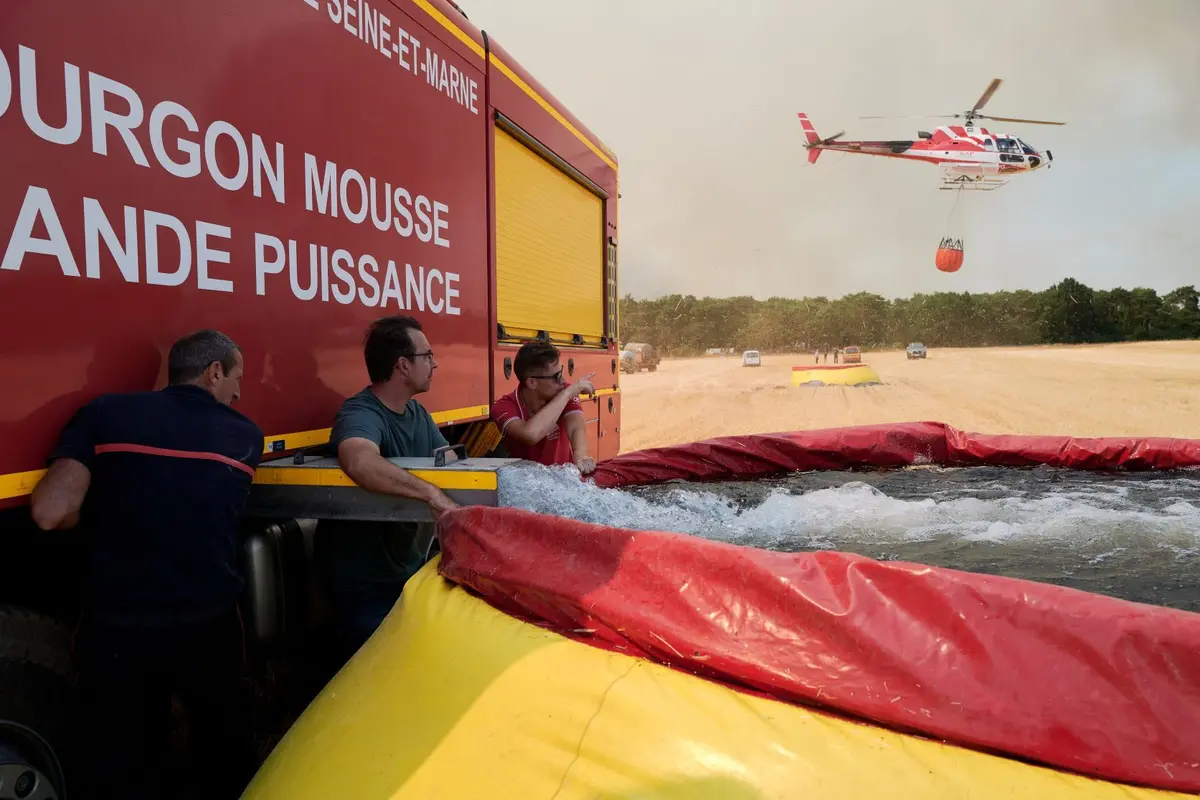 Firefighters and local farmers fill a temporary reservoir used by a firefighting helicopter collecting water with a suspended bucket after a wildfire broke out in the Fontainebleau Forest in Fontainebleau, France, on July 13, 2026. (Pierre Crom/Getty Images)
