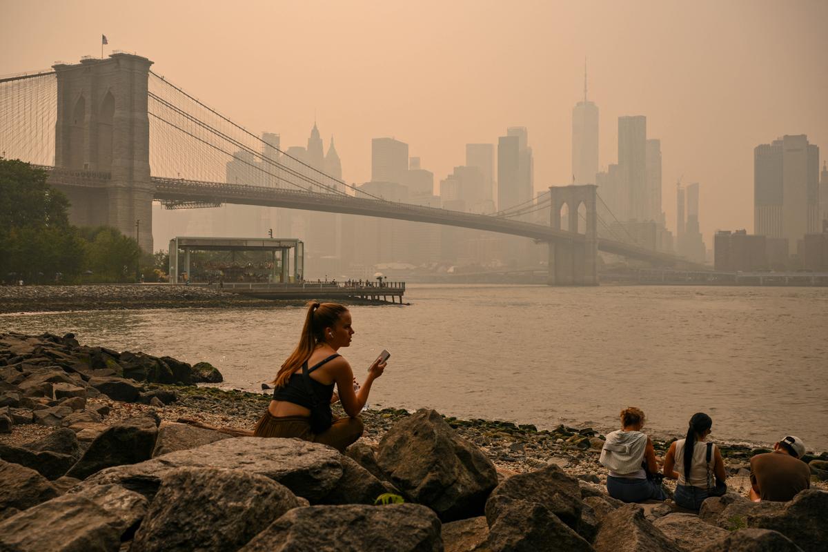 People sit near the Brooklyn Bridge as wildfire smoke from Canada causes hazy conditions in New York City on July 16, 2026. (Angela Weiss / AFP via Getty Images)