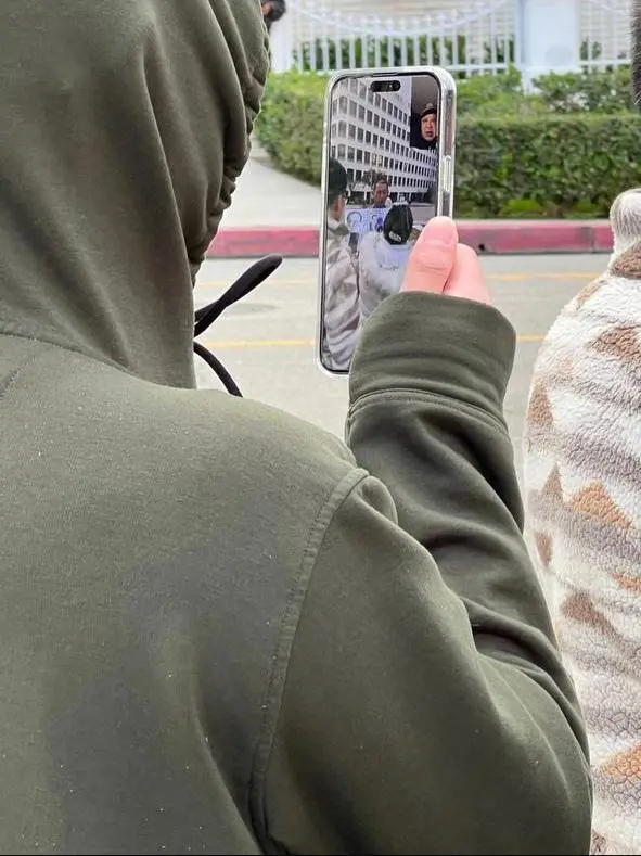 A hooded man livestreams Jie Lijian during a protest outside the Chinese Consulate in Los Angeles in December 2022. The phone screen shows a Chinese man wearing a police uniform on the other end of the call. (Courtesy of Jie Lijian)