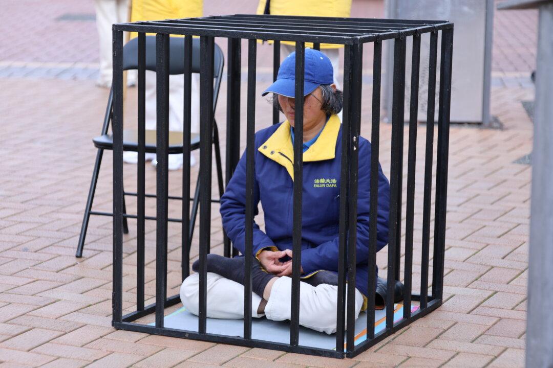 A lady sits inside a replica cage in a street demonstration symbolising the imprisonment and torture faced by adherents in China, during a rally in Wellington, New Zealand, on July 21, 2026. (Echo Wang/The Epoch times)