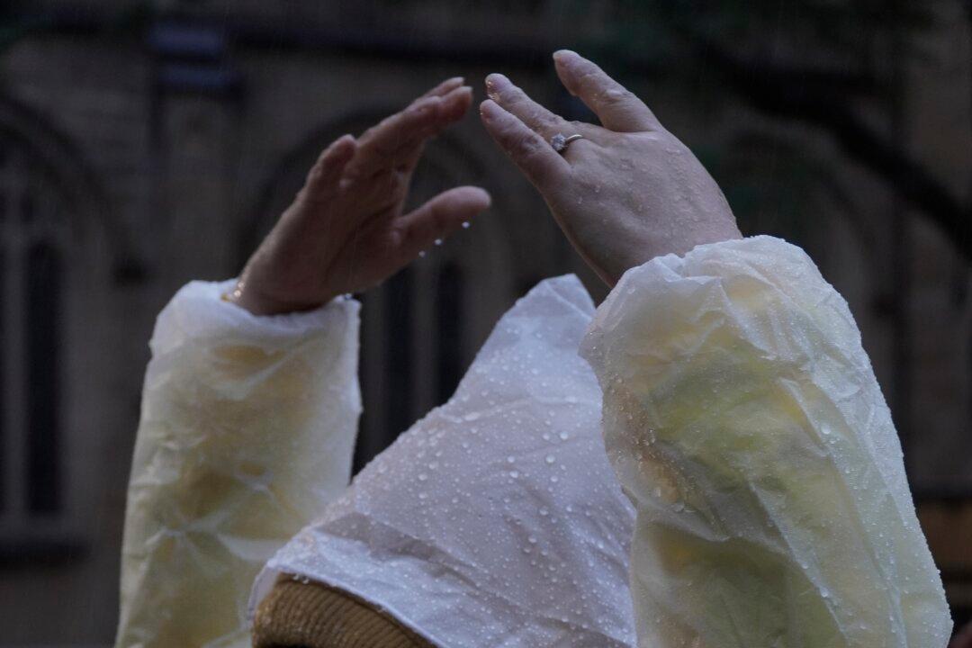 Braving the wet weather in a plastic raincoat, a practitioner continues the meditation exercises during a rally in Sydney on July 17, 2026. (Jason Lin/The Epoch Times)