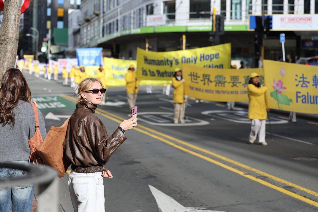 A bystander turns to capture photos as a Falun Dafa parade moves through Wellington, New Zealand, on July 21, 2026. (Echo Wang/The Epoch times)