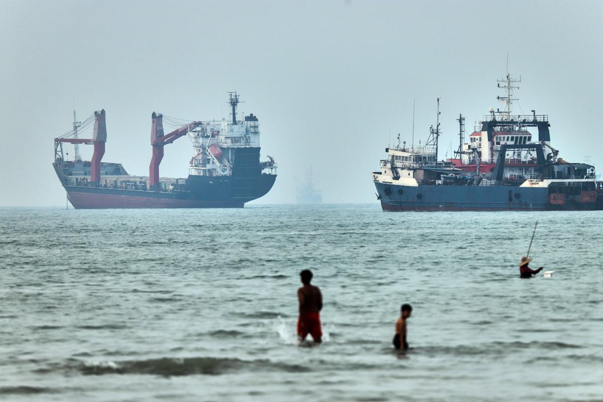 People wade in the water with cargo ships at anchor in the background, in the Strait of Hormuz off Bandar Abbas, Iran, on June 30, 2026. (Amirhosein Khorgooi/ISNA via AP)