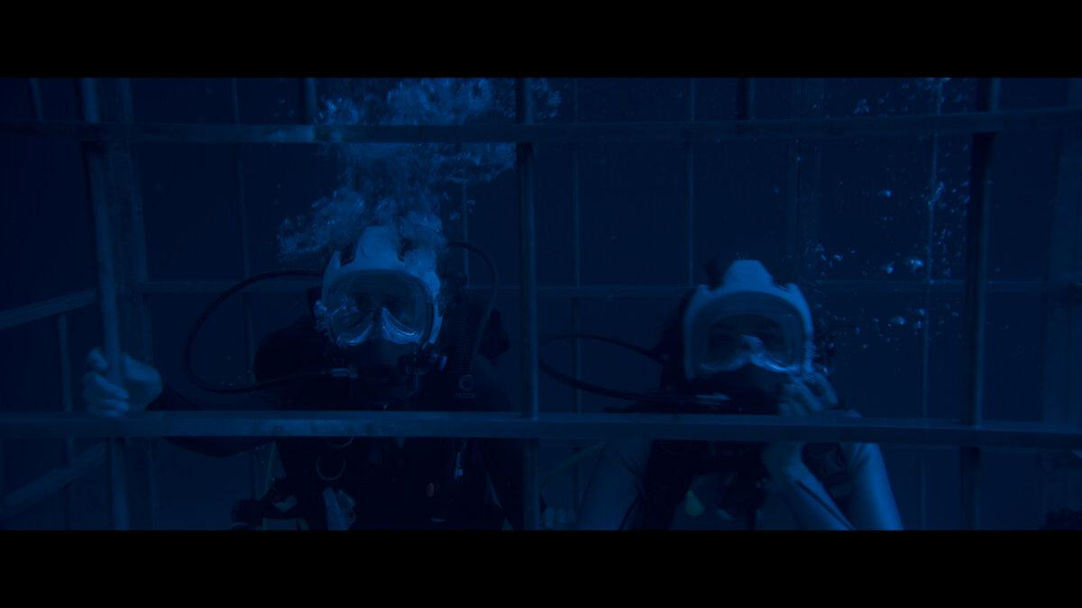 Tatiana (Laura Marano) and Kayle (Christina Ochoa) trapped in a shark cage, in “Above and Below.” (Aura Entertainment)