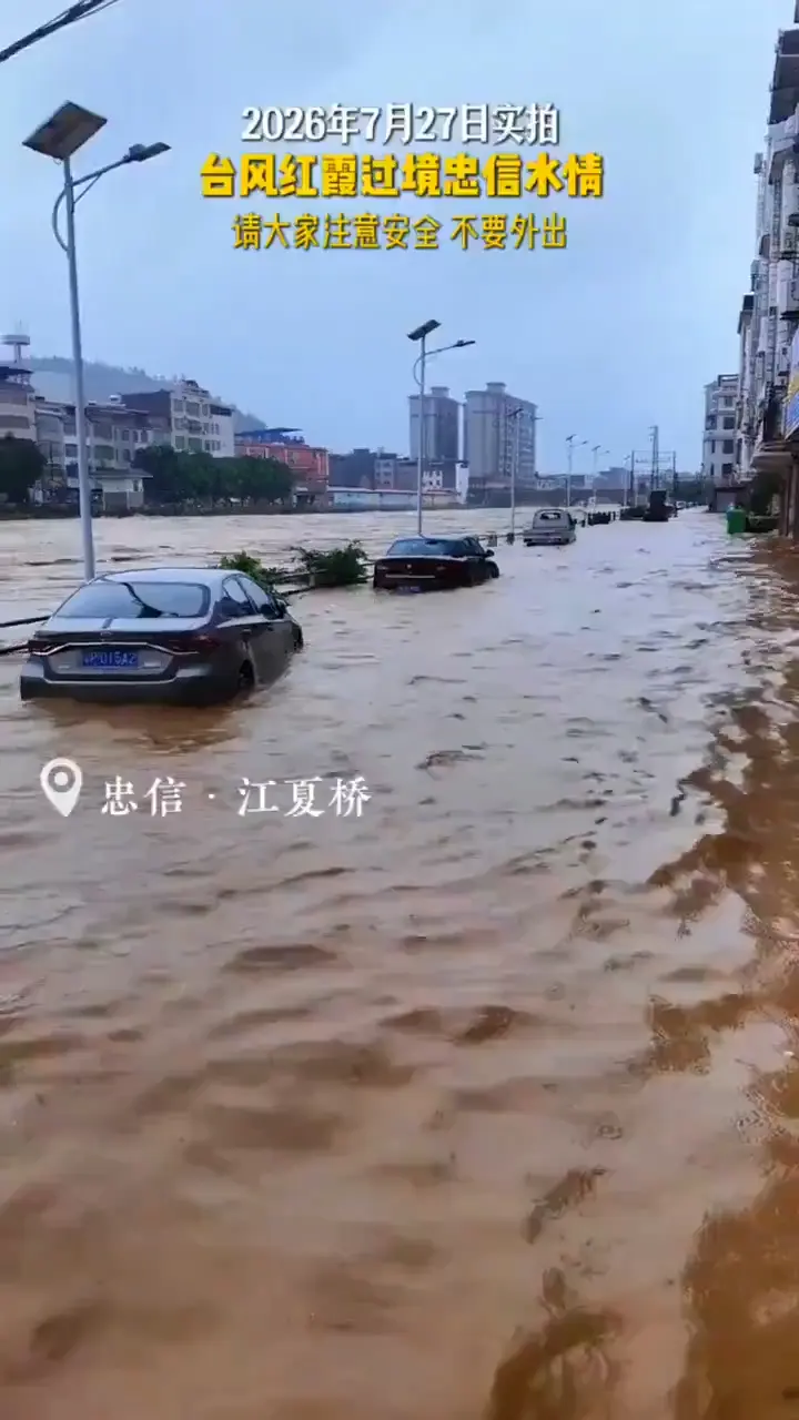 Floodwater covers a road and partially submerges vehicles near Jiangxia Bridge in Zhongxin Town, Lianping County, Guangdong Province, on July 27, 2026, as text on the resident-recorded video urges people to stay indoors, shared by citizen reporter Ying Tang. (Screenshot via The Epoch Times)