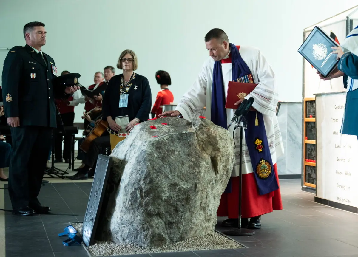 Then-Chaplain General Guy Chapdelaine places his hand on the rock centrepiece of the Kandahar cenotaph, located inside the Afghanistan Memorial Hall, during the cenotaph's rededication ceremony at National Defence Headquarters in Ottawa on Aug. 17, 2019. (The Canadian Press/Justin Tang)