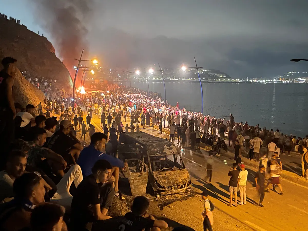 Migrants gather around a torched vehicle while waiting for a chance to cross to the Spanish enclave of Ceuta, on the Moroccan side of the border in Fnideq, Morocco, on July 31, 2026. (Ahmed El Jechtimi/Reuters)