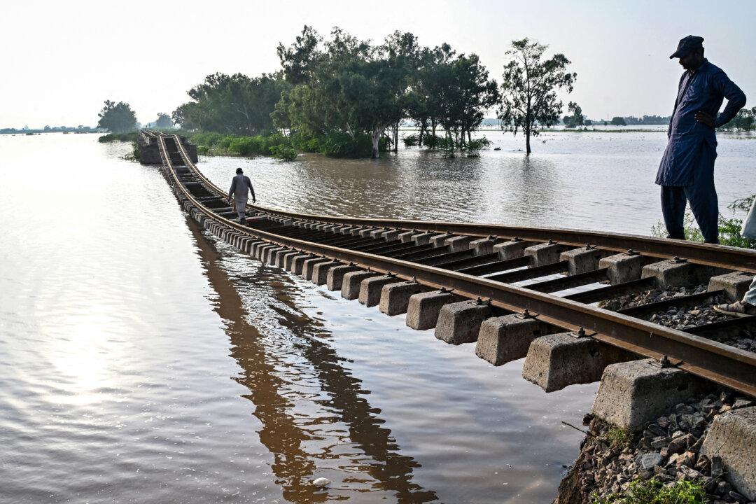 TOPSHOT - People walk over a damaged railway track in a flooded area after the Ravi River overflowed following heavy monsoon rains in Sheikhupura, in Pakistan's Punjab province on July 29, 2026. (Photo by Arif ALI / AFP via Getty Images)