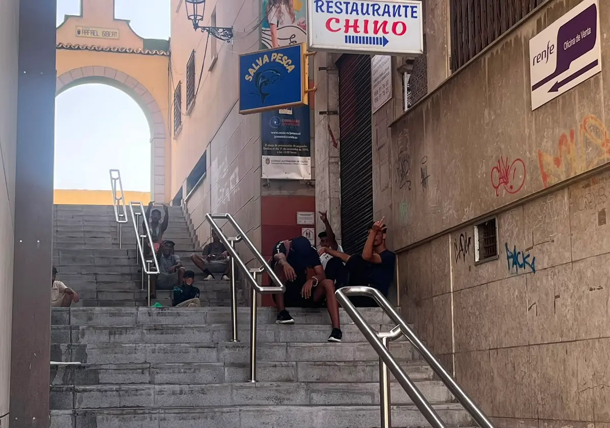 Moroccan illegal immigrants sit on the steps near the Rafael Gibert archway in Ceuta, Spain, on Aug. 1, 2026. (Etienne Fauchaire/The Epoch Times)