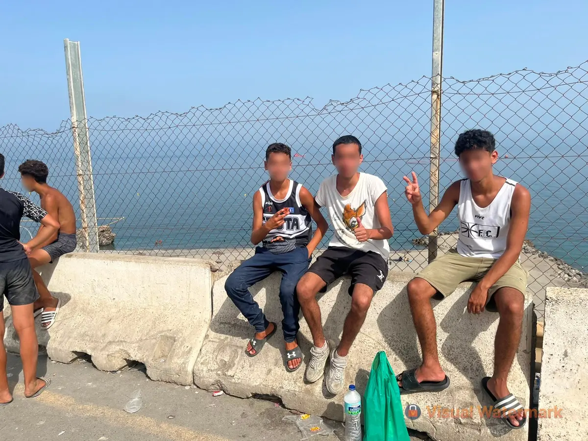 Three young Moroccans, Nazir (14), Wassim (15), and Yassine (15), sit by a fence overlooking the sea in Ceuta, Spain, on Aug. 1, 2026. (Etienne Fauchaire/The Epoch Times)