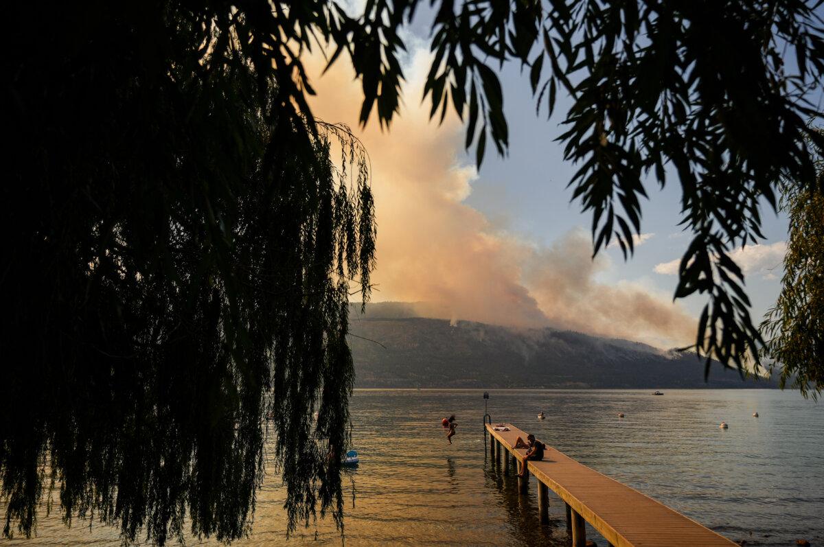A woman jumps off a dock into Okanagan Lake, in Lake Country, B.C., as the Quilpituk Creek wildfire burns on the mountainside across the lake near Fintry, on Aug. 3, 2026. (The Canadian Press/Darryl Dyck)