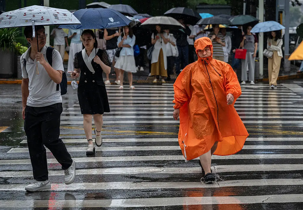 A commuter wears a rain poncho as she crosses a street during a rainstorm caused by Typhoon Dolphin in Beijing on Aug. 12, 2026. (Kevin Frayer/Getty Images)