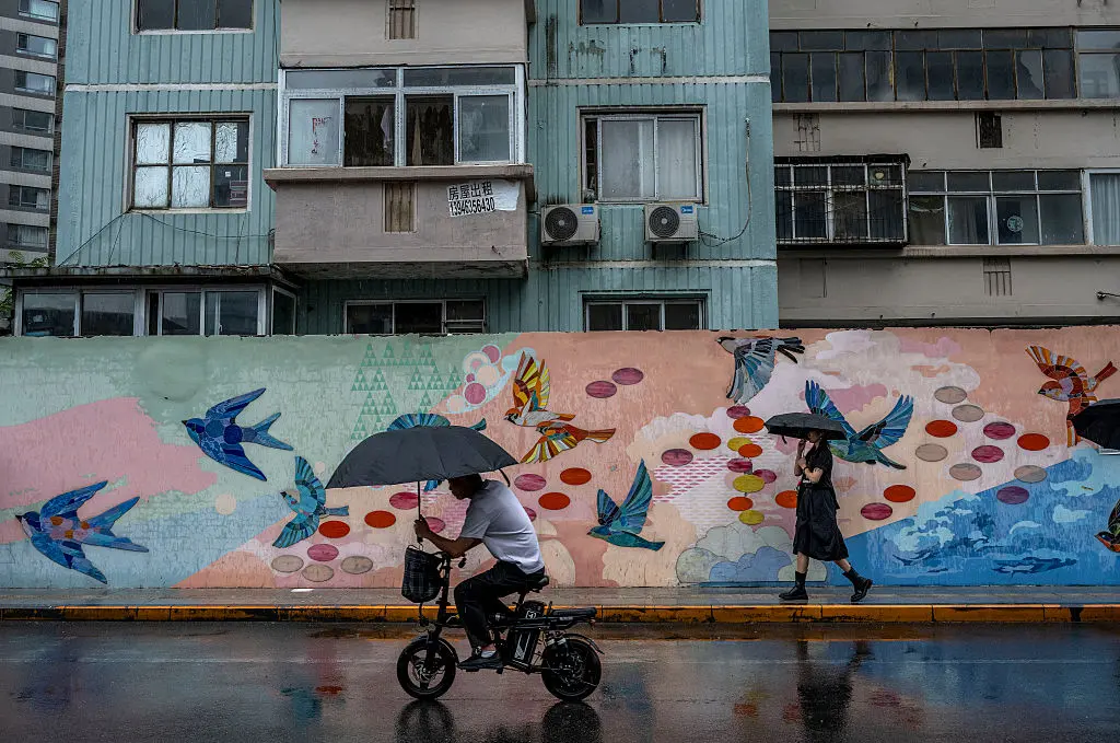 A man holds an umbrella as he rides on an electric scooter during a rainstorm caused by Typhoon Dolphin in Beijing on Aug. 12, 2026. (Kevin Frayer/Getty Images)