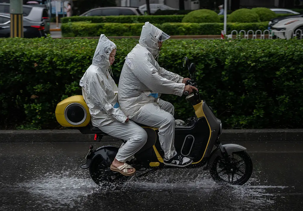 Commuters wear rain suits as they ride on an electric scooter during a rainstorm caused by Typhoon Dolphin in Beijing on Aug.12, 2026. (Kevin Frayer/Getty Images)