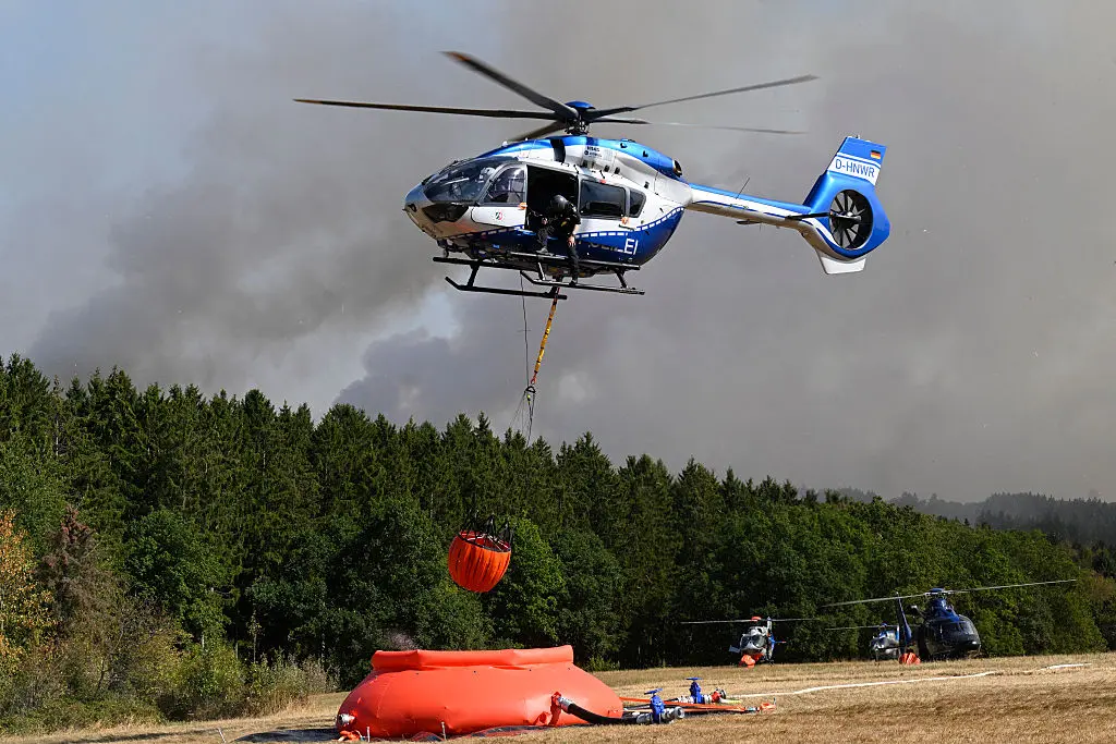 Police helicopters load water to fight a forest fire in Huertgenwald, western Germany on Aug. 14, 2026. Around 1,800 people had to leave their homes in western Germany overnight as a wildfire spread nearby, officials said, with helicopters and army equipment deployed to help battle the flames. (Roberto Pfeil/AFP via Getty Images)