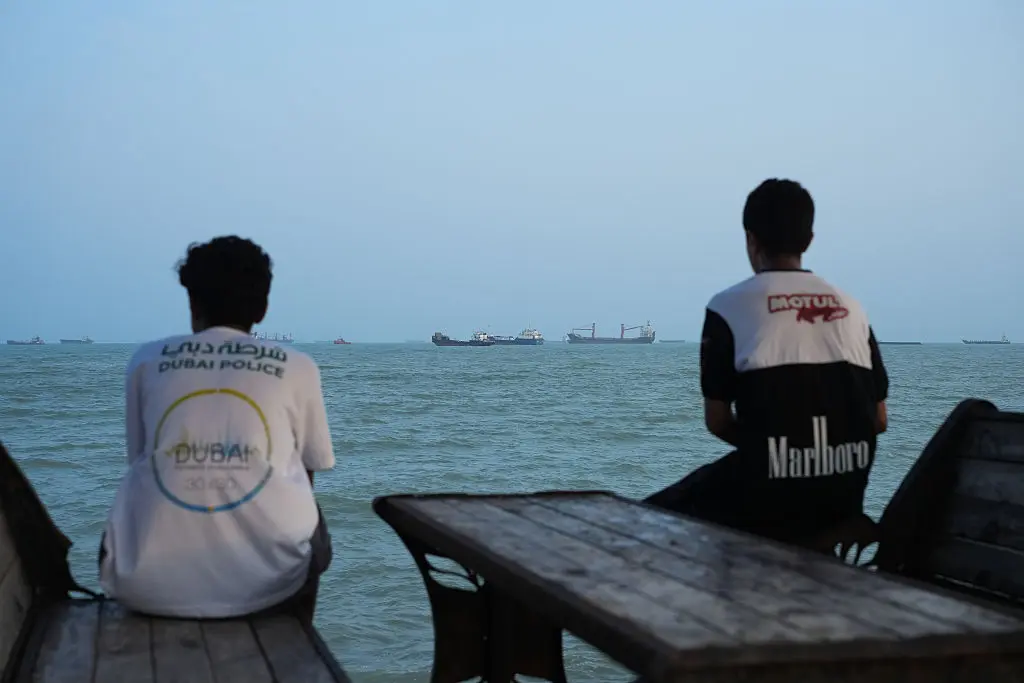 Two youths sit on the shoreline as ships are seen anchored in the Strait of Hormuz off the coast of Bandar Abbas, Iran, on Aug. 10, 2026. (Ali Saeedi/Getty Images)