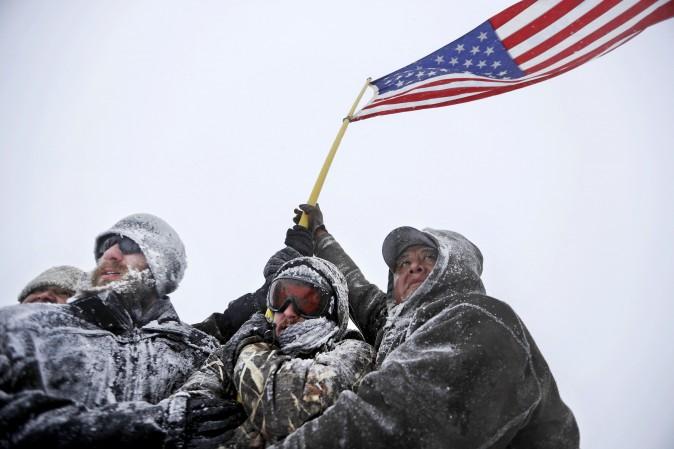 Military veterans huddle together holding a U.S. flag against strong winds during a march outside the Sacred Stone Camp, where people have gathered to protest the Dakota Access Pipeline, near Cannon Ball, N.D., on Dec. 5. (AP Photo/David Goldman)