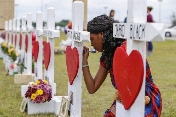 Santa Fe High School freshman, Jai Gillard writes messages on each of the 10 crosses representing victims in front the school in Santa Fe, Texas, on May 21, 2018. (Steve Gonzales/Houston Chronicle via AP)