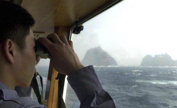 A South Korean coastguard looks at Dokdo islets, known as "Takeshima" in Japanese, through a telescope on the patrol ship Sambong-ho on the East Sea, South Korea, on April 28, 2005. (AP Photo/Ahn Young-joon, File)