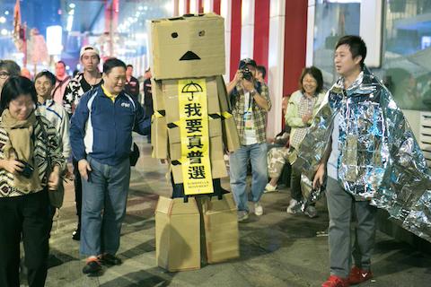 A person dressed inside cardboard boxes walks around in the Mong Kok protest site with a the main banner that reads "We want universal suffrage," in Hong Kong on Nov. 13, 2014. (Benjamin Chasteen/Epoch Times)