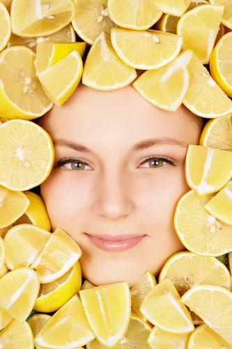 The detoxifying action of drinking lemon water will release impurities through every exit point (or detoxification channel), including skin. (<a href="http://www.shutterstock.com/pic-117781243/stock-photo-woman-beauty-face-with-lemons.html?src=fIppU3bTNxgoy9XhRS76RQ-1-27" target="_blank" rel="noopener">Shutterstock</a>)