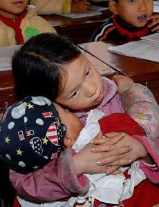 Ning Yuexiang pays attention in class while coaxing her brother to sleep. (The Epoch Times Archive)