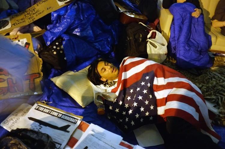<a><img src="https://www.theepochtimes.com/assets/uploads/2015/09/129042731ii.jpg" alt="Wall Street protesters rest in Zuccotti Park where hundreds of other activists are living on October 11, 2011 in New York City. (Spencer Platt/Getty Images)" title="Wall Street protesters rest in Zuccotti Park where hundreds of other activists are living on October 11, 2011 in New York City. (Spencer Platt/Getty Images)" width="575" class="size-medium wp-image-1796399"/></a>