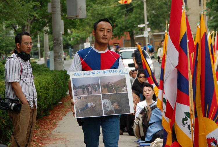 A Tibetan demonstrator walks in front of the Chinese consulate in Toronto in June 2008 with a placard around his neck showing Chinese military shooting Tibetans with exploding bullets. (Matthew Little/EpochTimes)