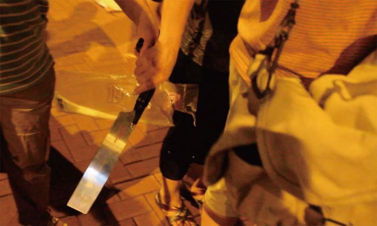 A female member of the Hong Kong Youth Care Association takes a large chopping knife from another member, preparing to use it to threaten a NTD Television reporter. (The Epoch Times)