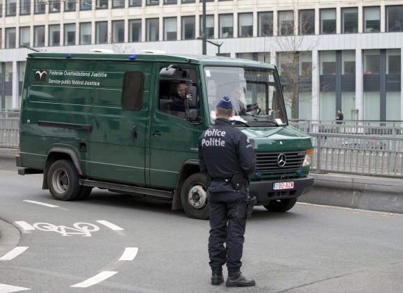 A police officer stands guard as a convoy thought to be containing attacks suspects arrives outside the federal court building in Brussels on Thursday, April 14, 2016. (AP Photo/Virginia Mayo)