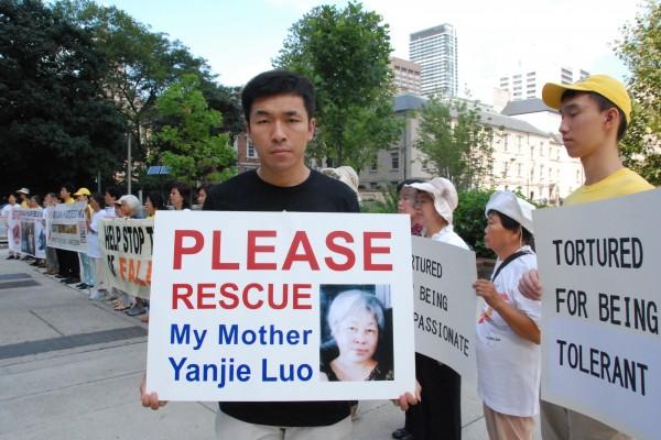 Wenta Fan holds a sign with a portrait of his mother, Yanjie Luo, who in 2011 was sentenced to 13 years in prison in China for practicing Falun Gong, outside Toronto City Hall on Aug. 25, 2016.  (Yi Ling/Epoch Times)