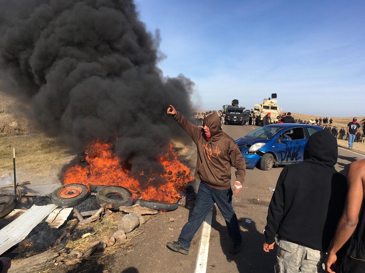 Demonstrators stand next to burning tires as armed soldiers and law enforcement officers assemble on Oct. 27, 2016, to force Dakota Access pipeline protesters off private land where they had camped to block construction. (Mike McCleary/The Bismarck Tribune via AP)