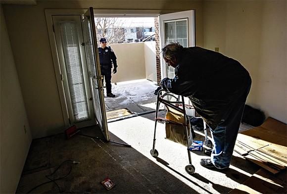 An officer waits to escort Harvey Lesser, an unemployed software developer, from his apartment after serving him with a court order for eviction in Boulder, Colo., on Dec. 11, 2009.