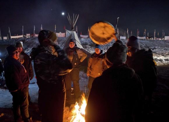 Campers gather around a fire to sing and drum traditional Native American social songs at the Oceti Sakowin camp where people have gathered to protest the Dakota Access oil pipeline in Cannon Ball, N.D., on Dec. 4, 2016. (AP Photo/David Goldman)