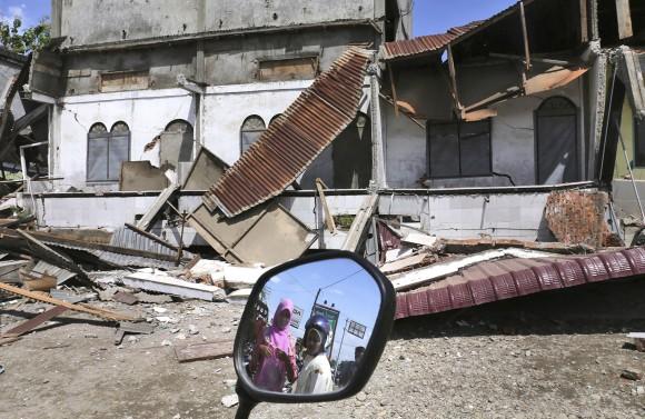 Women are reflected in a motorbike's mirror as they access the damaged building after an earthquake in Pidie Jaya, Aceh province, Indonesia, on Dec. 7, 2016. (AP Photo/Heri Juanda)